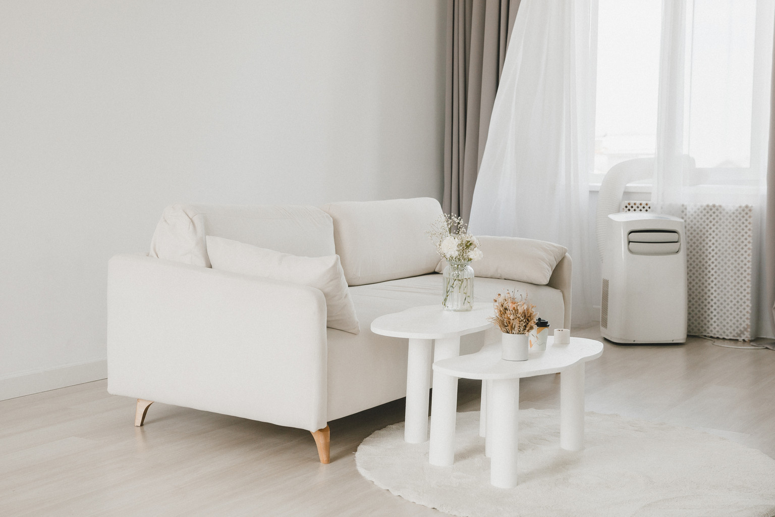 Helles Wohnzimmer mit weißem Sofa und einem Klimagerät am Fenster.